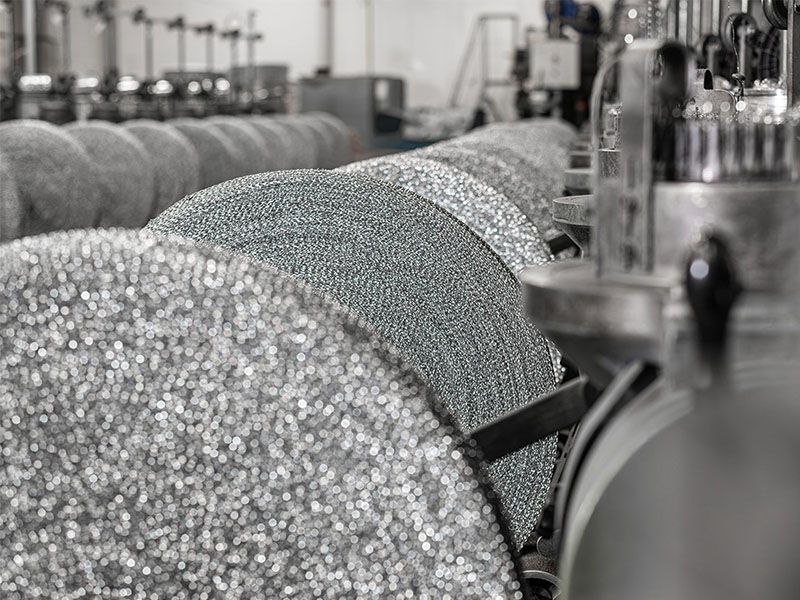 Mehrere zylindrische Rollen aus Metallgestrick auf einer industriellen Produktionsanlage